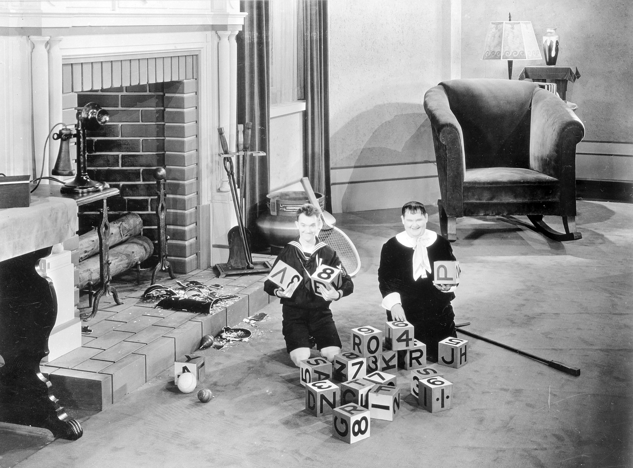 Stan Laurel and Oliver Hardy playing with giant building blocks as they appear in 'Brats', directed by James Parrott, in which they play their own sons, 1930.