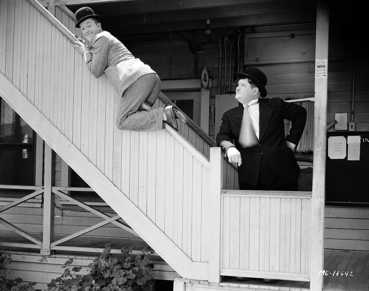 Oliver Hardy looks on unimpressed as Stan Laurel slides down a bannister. They are clowning around behind the scenes on the Hal Roach lot, 1930.