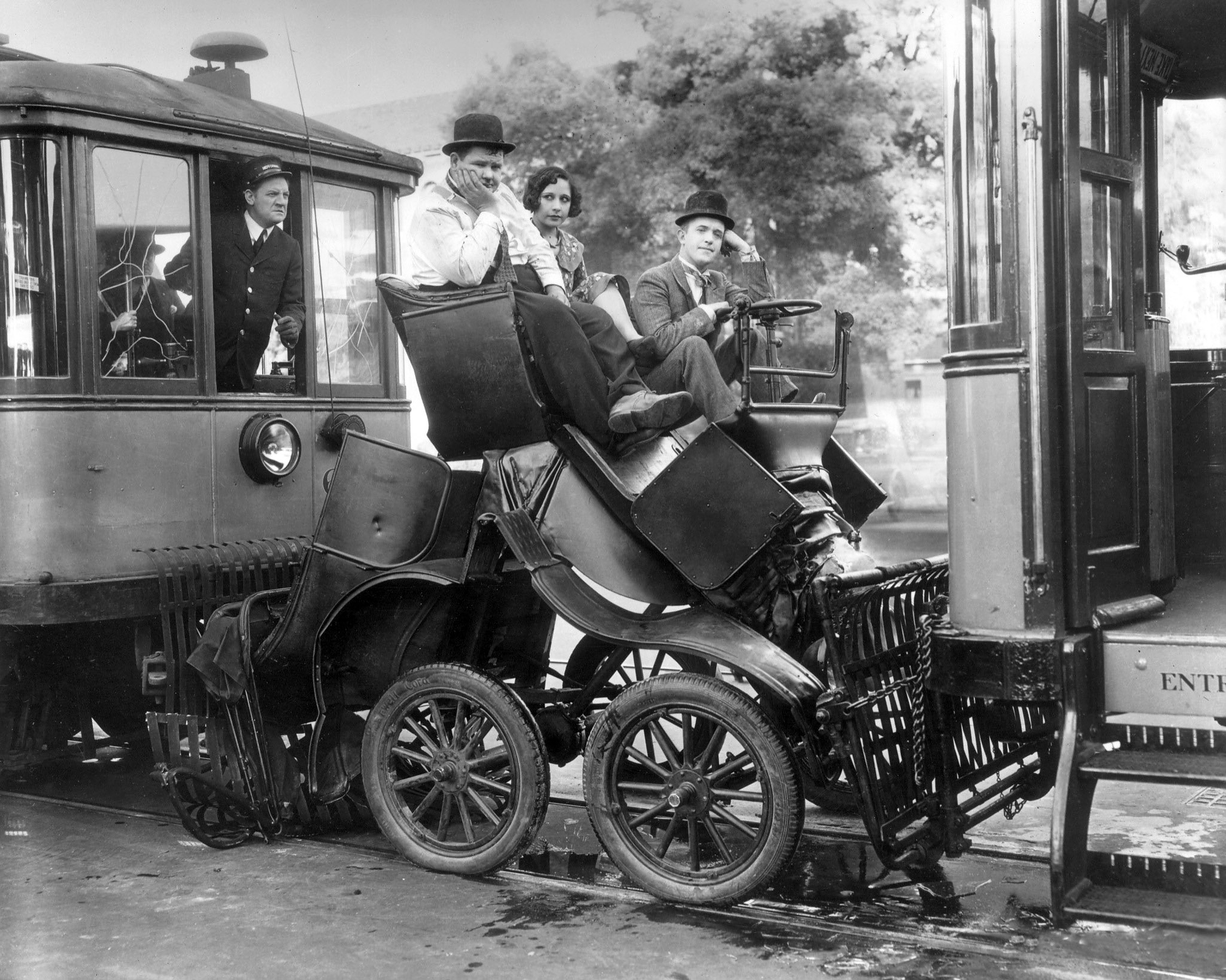 American actor Oliver Hardy and British-born actor Stan Laurel sit in an automobile sandwiched between two trolley cars in a still from director James Parrott's film, 'Hog Wild'. Charles McMurphy plays the streetcar conductor while another actor, possibly Dorothy Granger sits in the car, 1930.