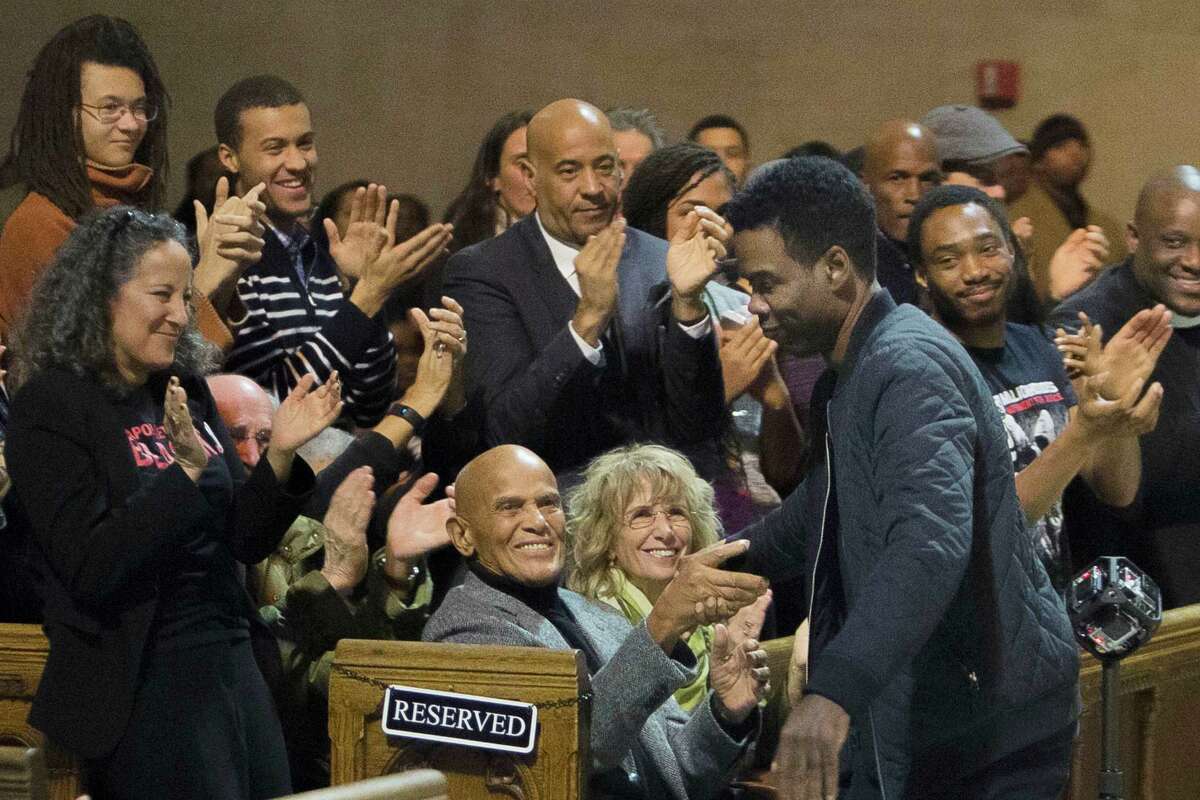 In this Monday, Jan. 18, 2016 photo, Comedian Chris Rock, center right, shakes hands with singer and social activist Harry Belafonte, center left, during an event celebrating the life and legacy of Dr. Martin Luther King Jr. at the Riverside Church in New York. Rock, who is scheduled to host the Oscars Feb. 28, has unveiled a new promotion for the broadcast, calling the ceremony "The White BET Awards." (AP Photo/Andres Kudacki)