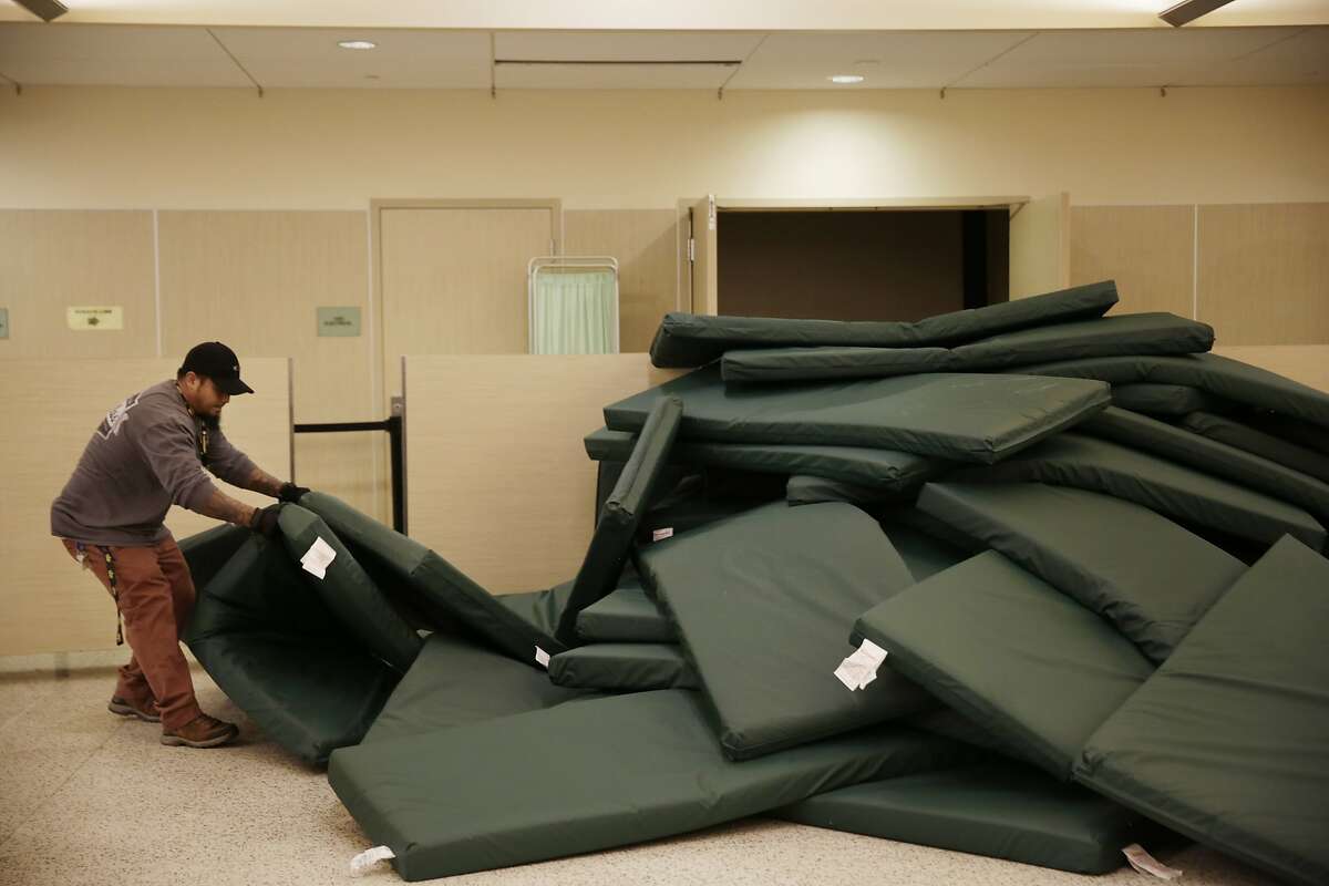 Rath Nou, shelter staff, picks up mats as he begins to arrange the beds in the evening for clients at the St. Anthony's emergency winter shelter on Tuesday, January 19, 2016 in San Francisco, Calif.