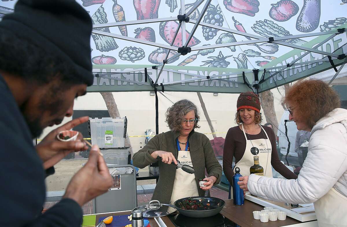 Left to right--Art student Shawn Edgley (left) has a sample of sautŽed chard while Lia Hillman cooks with library page Morgan McGuire (wearing cap), and cookbook librarian Ruth Amernick (right) passes out samples at the farmer's market in the Civic Center in San Francisco, California, on Thursday, January 20, 2016.