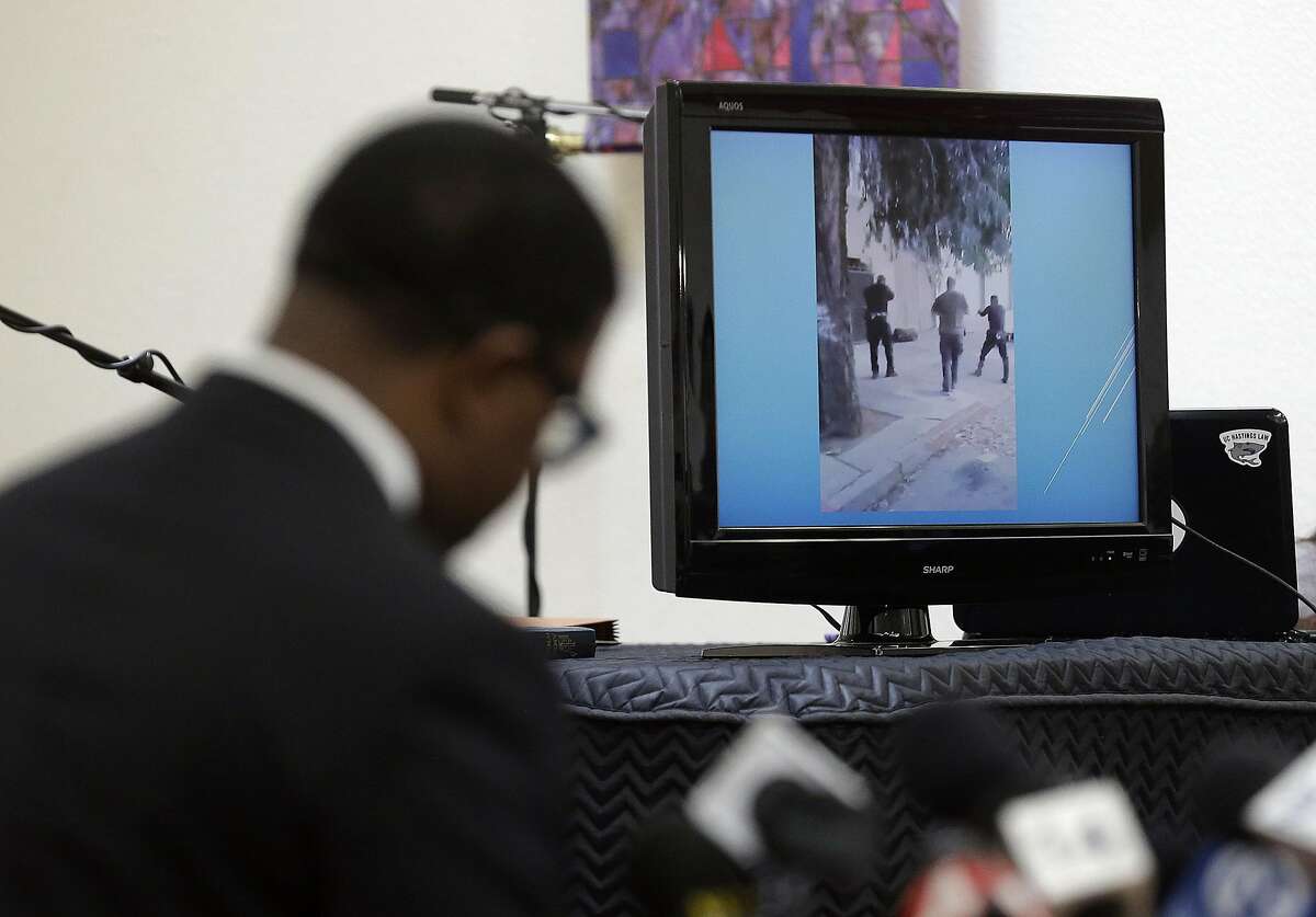 Attorney Adante D. Pointer, left, speaks at a news conference in San Francisco, Monday, Jan. 18, 2016, as a video is displayed of the San Francisco police shooting of Mario Woods who police say appeared to raise a knife and approach one of the officers. The family of Woods has asked the U.S. Department of Justice to investigate the officers who shot Woods on Dec. 2, 2015, and review the San Francisco police department's use of deadly force, stops, and detention and searches of African American and Latinos citizens for possible civil rights violations. (AP Photo/Jeff Chiu)