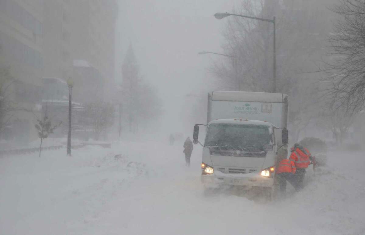 As the snow blows, a crew works to free a truck stuck in the snow, Saturday, Jan. 23, 2016 in Washington. A blizzard with hurricane-force winds brought much of the East Coast to a standstill Saturday, dumping as much as 3 feet of snow, stranding tens of thousands of travelers and shutting down the nation's capital and its largest city.