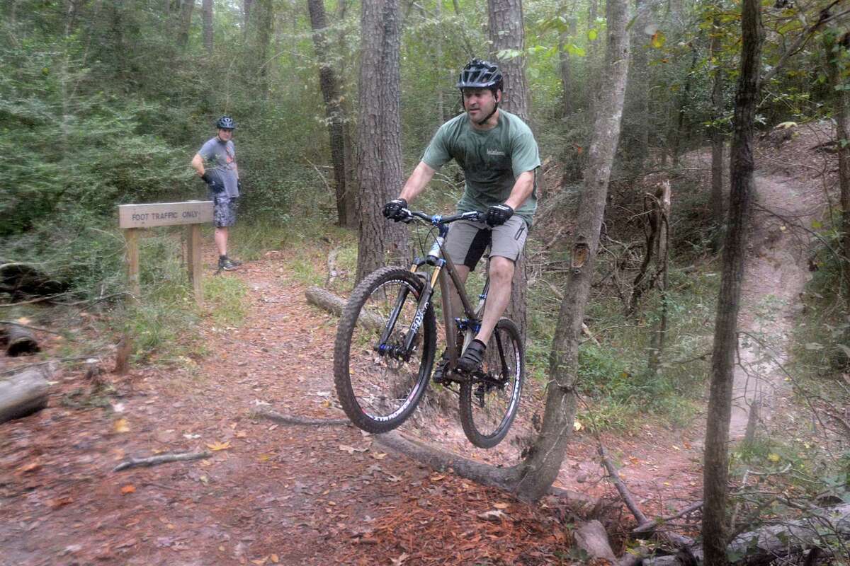 Cypress resident Mitch Callihan jumps an obstacle, after cycling through a creek on bike trails at the 100 Acre Wood Preserve, 10602 Normont. The preserve has two miles of trails through rolling, forested terrain. Watching is Bill Collier, incoming president of the Greater Houston Off Road Bicycle Association.