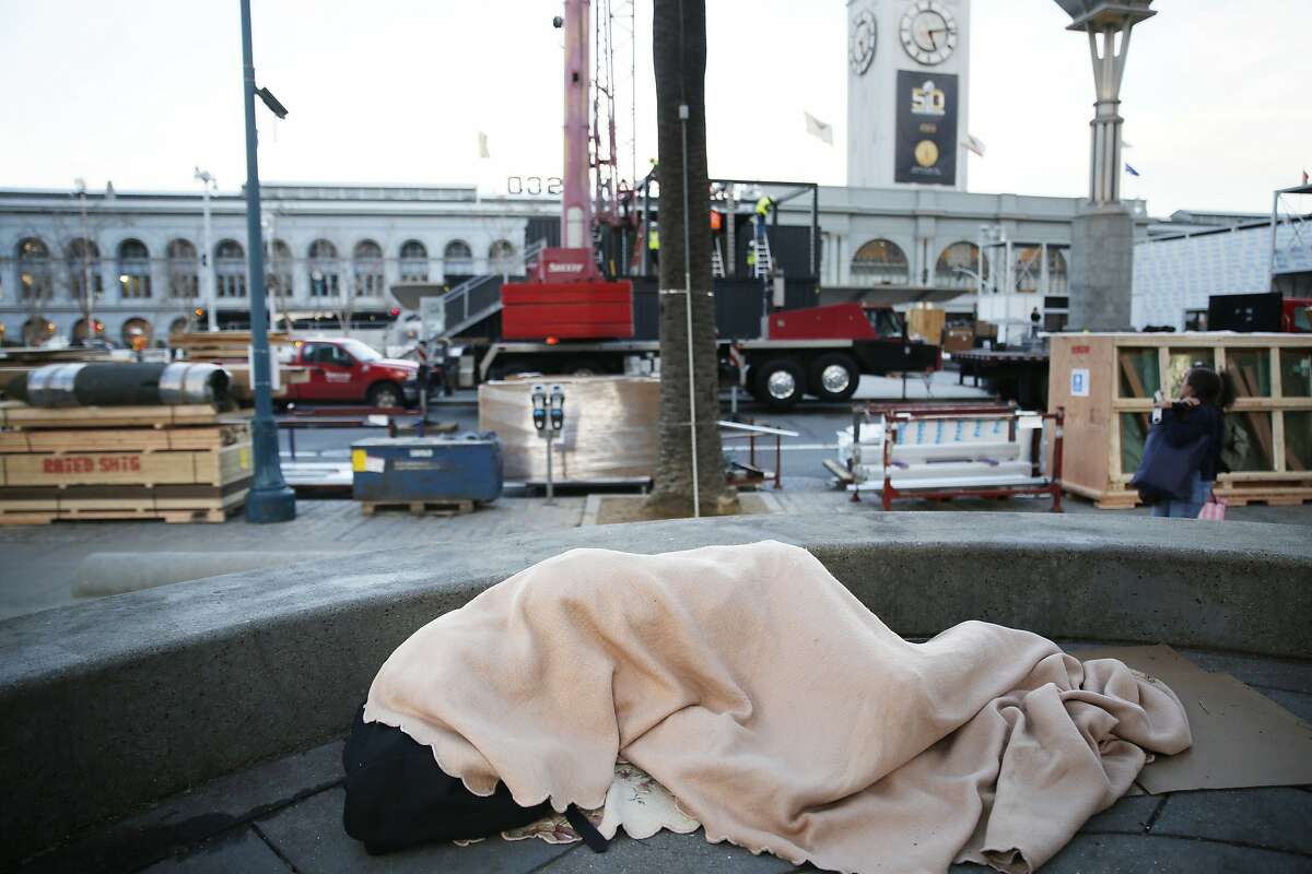 Selassie Sereño, sleeps on the ground under a blanket along the Embarcadero as the Super Bowl City begins to be built around her on Monday, January 25, 2016 in San Francisco, Calif.