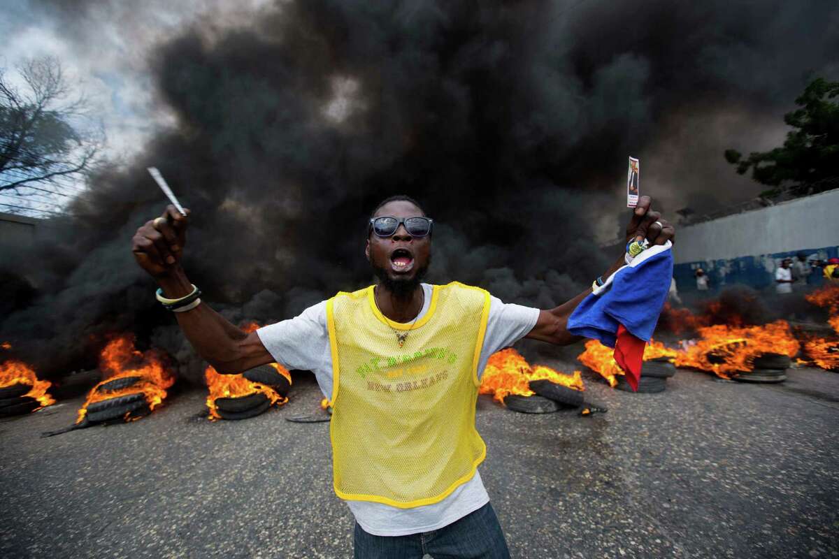 An anti-government demonstrator holds up a picture of former president Jean Bertrand Aristide as he demand the president's resignation in Port-au-Prince, Haiti, Saturday, Feb. 6, 2016. Top Haitian leaders negotiated an agreement to install a short-term provisional government less than 24 hours before President Michel Martelly was scheduled to step down, an official with the Organization of American States and local authorities announced Saturday. (AP Photo/Dieu Nalio Chery)