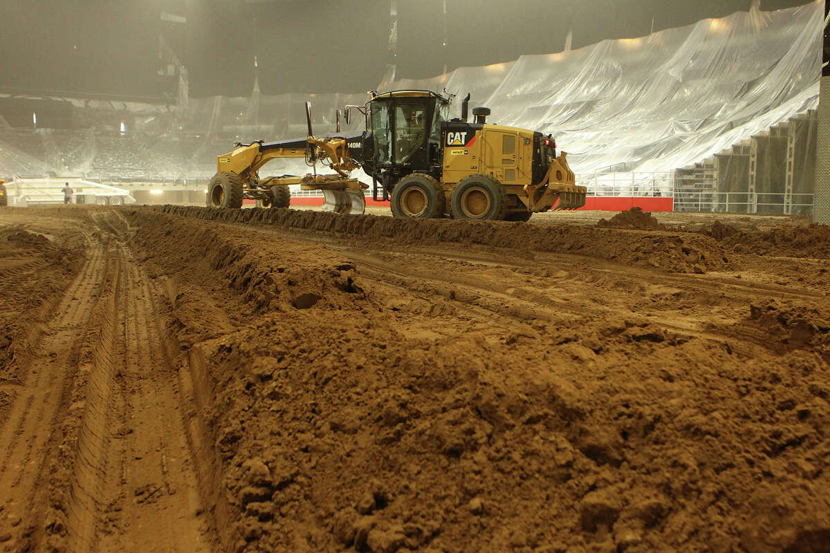 A grader operator spreads dirt in the AT&T Center in preparation for the rodeo, which opens Thursday.