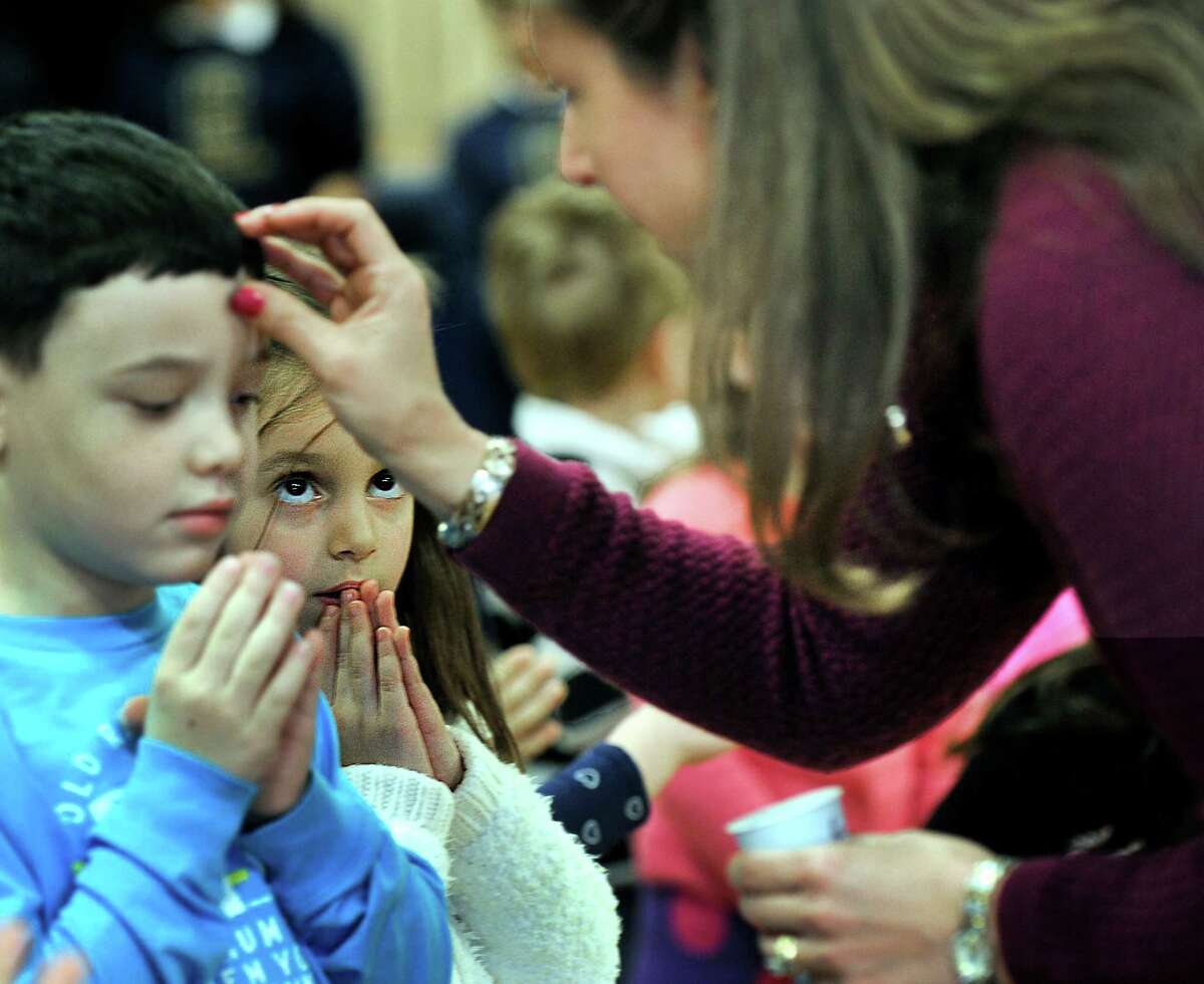Haylee Palmer, pays close attention, as teacher assistant and Eucharistic Minister Janette Buonaiuto places ashes on Isaac Leone's forehead. The children, kindergartners at St. Gregory the Great Catholic School in Danbury, observe Ash Wednesday with an all-school assembly Wednesday, Feb. 10, 2016.