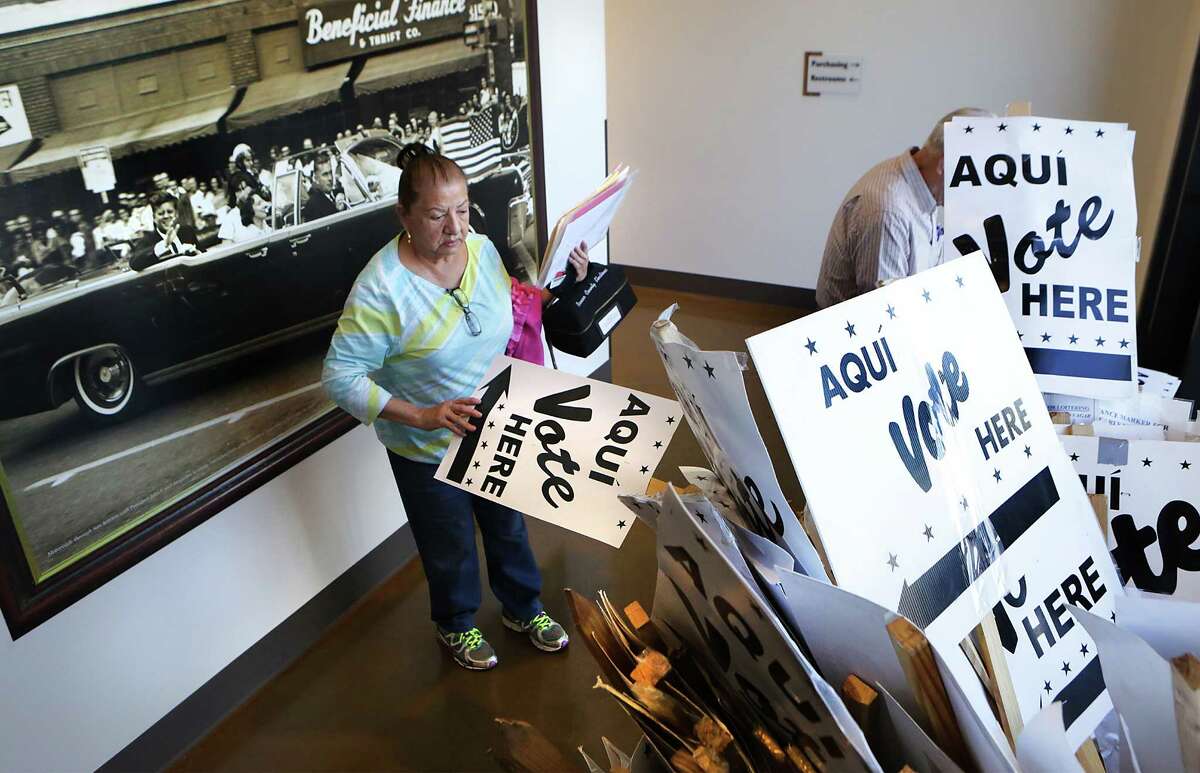 Esther Gill, a co-judge at a precinct in East Central, picks up extra signs following a training session for Bexar County election officials at Bexar County Election Department on Friday, Feb. 12, 2016. Behind Gill is a photo of John F. Kennedy's motorcade as it travels through downtown San Antonio the day before he was killed in Dallas.