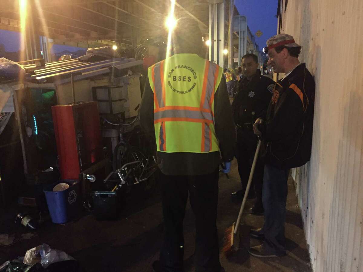 A man who identified himself as Tennessee, right, takes a break from sweeping to speak with a city worker outside of his trailer at a homeless encampment on Division Street in San Francisco on Thursday.