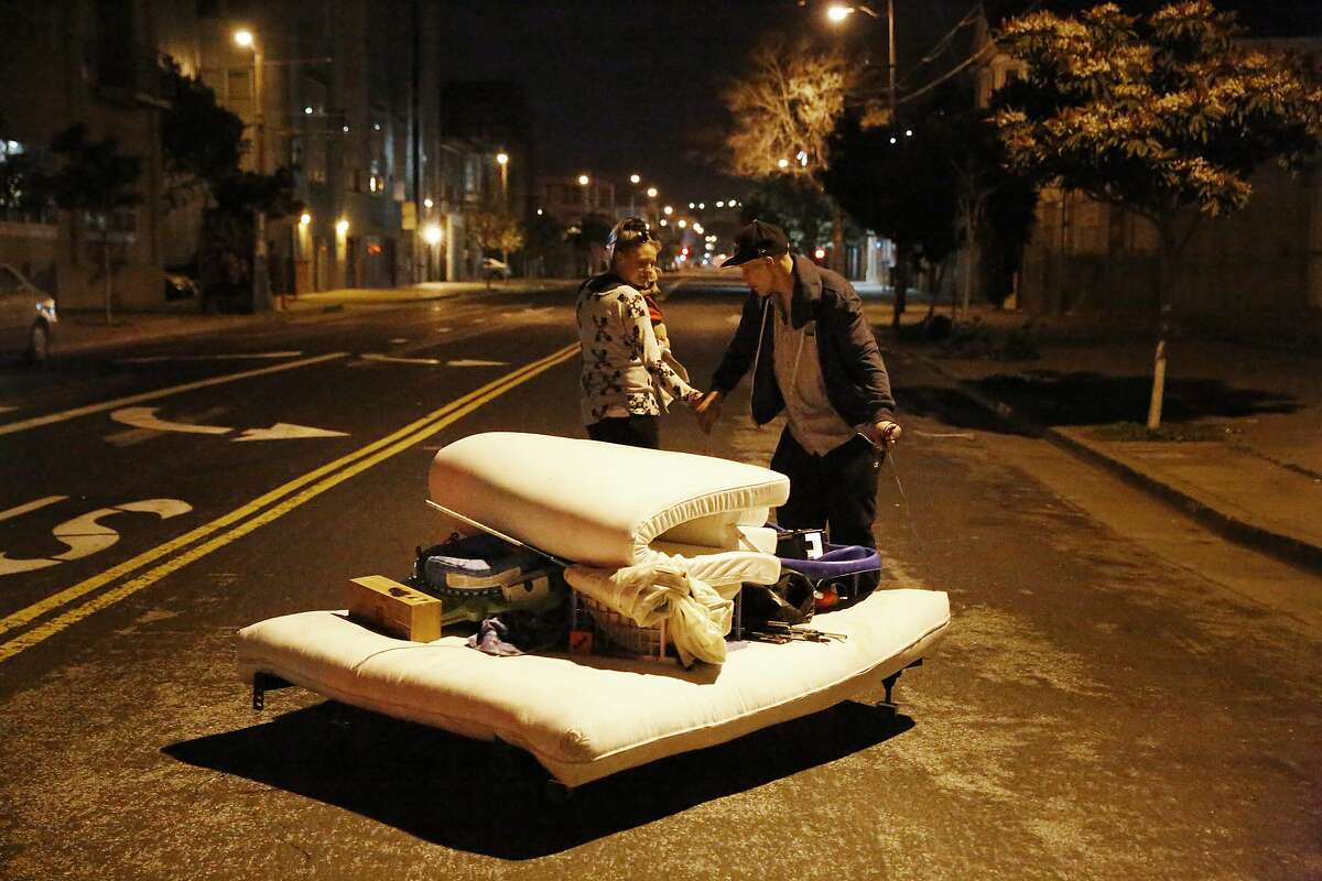 Heather Brown (left) carries her dog Baby Belle as she and fiance Travis Perot pull their mattress and belongings up 12th Street from 13th Street early Friday in advance of a homeless sweep that hadn’t arrived by the deadline.