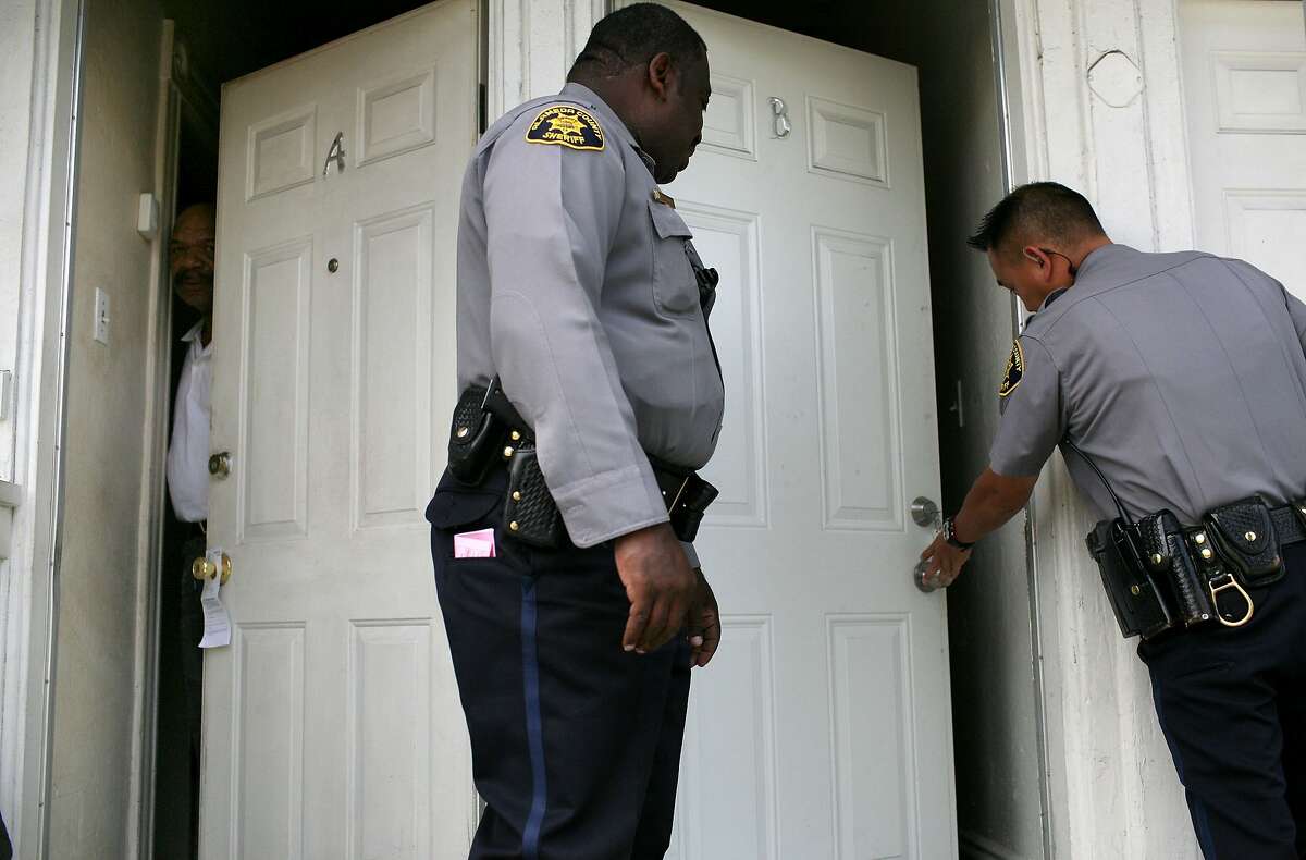 A neighbor peers out of his door as Alameda County Sheriff deputies enter an apartment to evict tenants in Oakland in 2009.