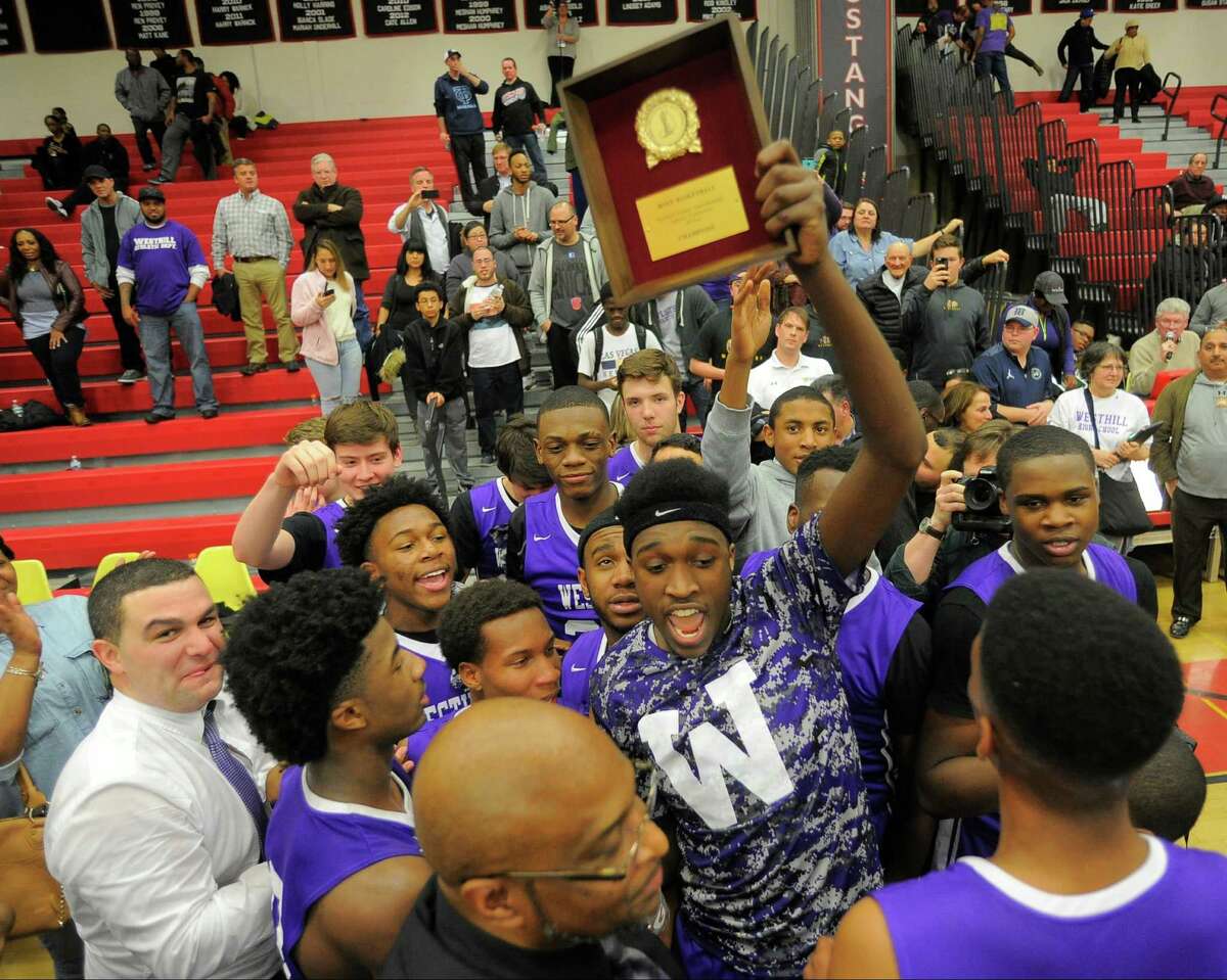 Westhill Lenold August holds the championship plaque as his team celebrates their win over Danbury. Westhill defeated Danbury 72-61 in an FCIAC basketball championship at Fairfield Warde High School in Fairfield, Conn. on March 3, 2016.