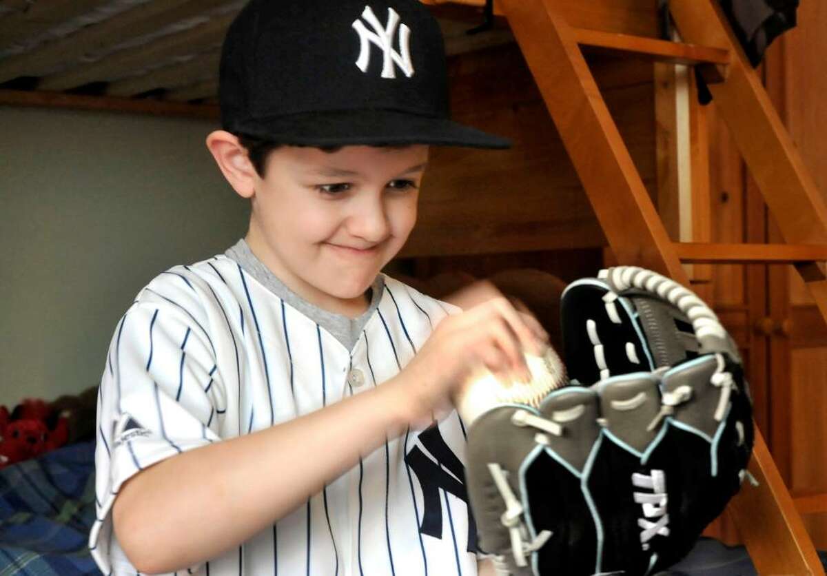 Caleb Schlissel, 6, works his glove in preperation for baseball season, in the bedroom of his Danbury home, on Friday, Feb.19,2010.