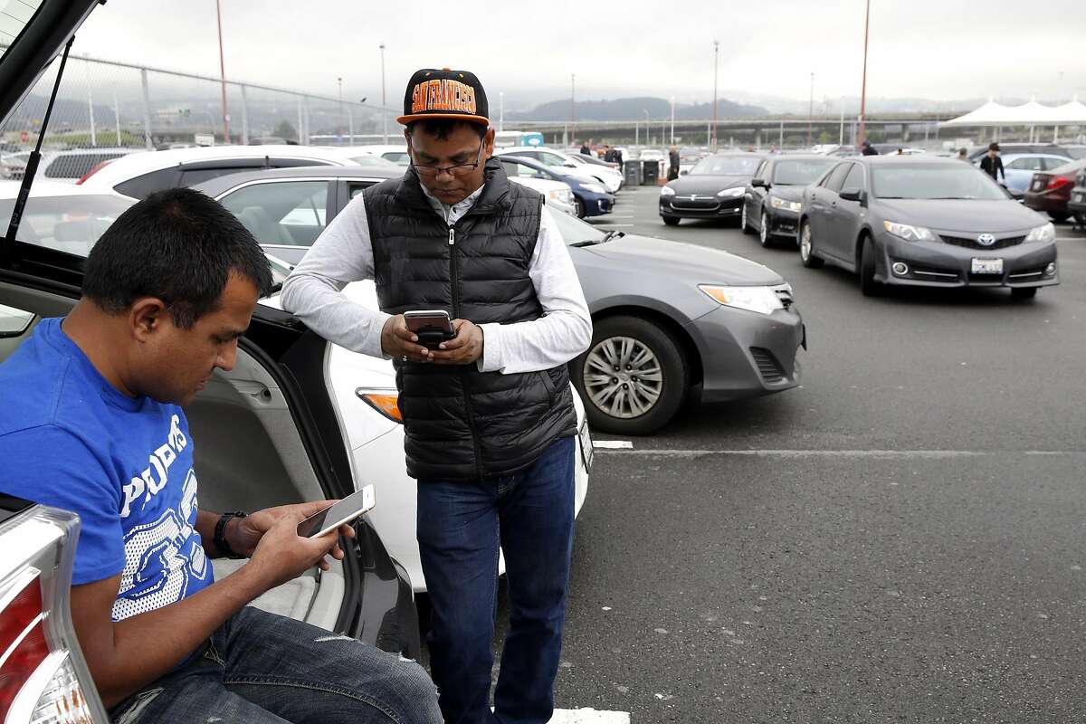 Uber drivers Madan Shrestha (left) and Om Adhikari chat while waiting for calls in the TNC lot at San Francisco International Airport in San Francisco, California, on Wednesday, March 9, 2016.