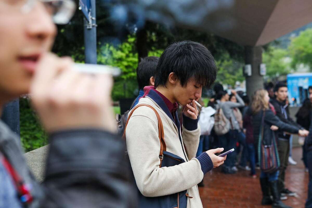 Yuto Takita, 23, (center) scrolls through his phone while smoking a cigarette at UC Berkeley, in Berkeley, California, on Thursday, March 10, 2016.