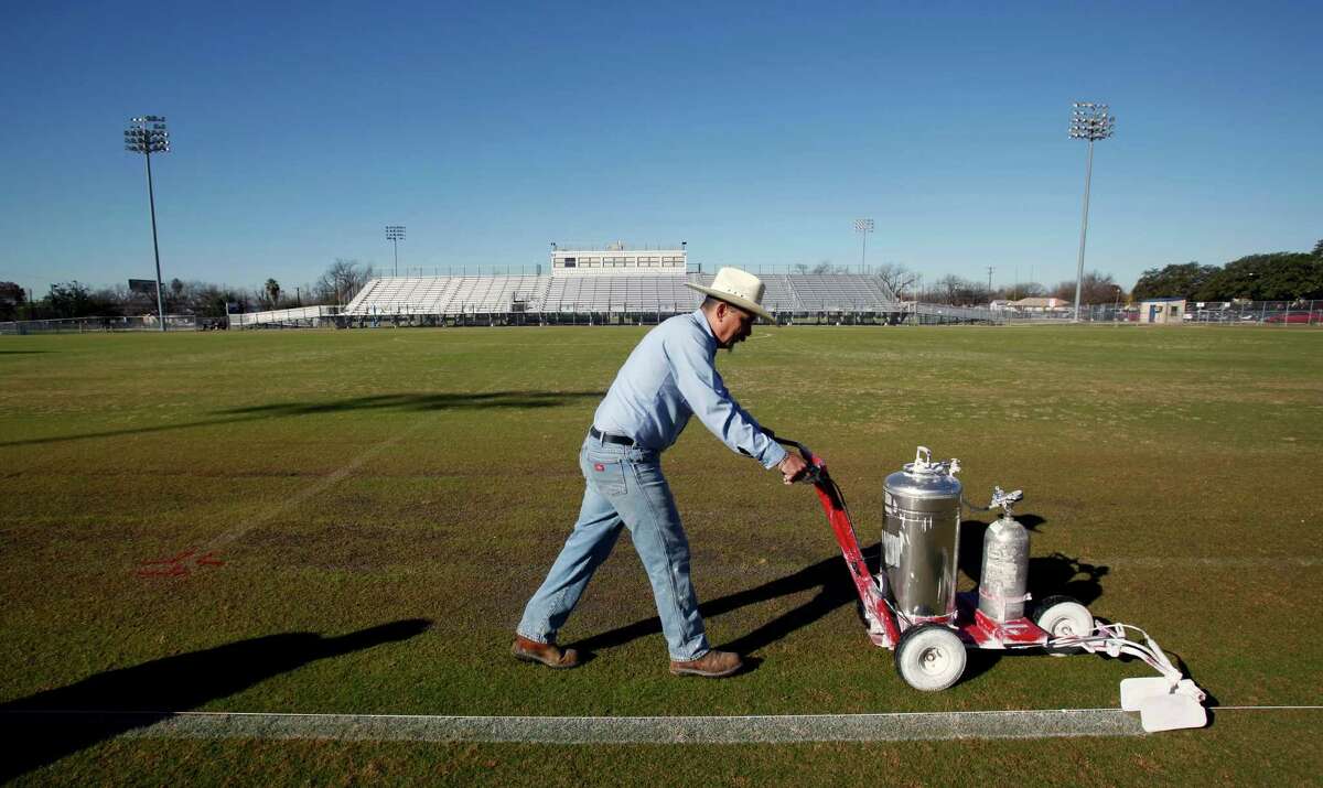 In this file photo, a San Antonio Independent School District athletics department maintenance worker Daniel Thatcher paints stripes on a field at the SAISD sports complex. Community activists are pushing the district to pay all workers a living wage.