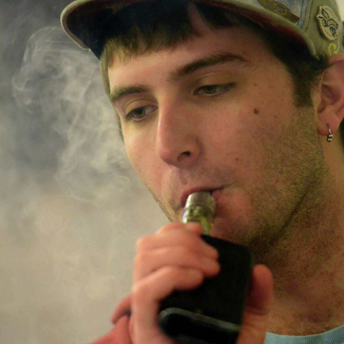 E-Stop E-Cigs co-owner Aidan Belmont vapes while at the shop on Post Road in Milford, Conn. The Ansonia Board of Aldermen decidede not to include vaping in a ban prohibiting smoking and chewing tobacco products in the city’s parks, recreational sites and athletic fields.