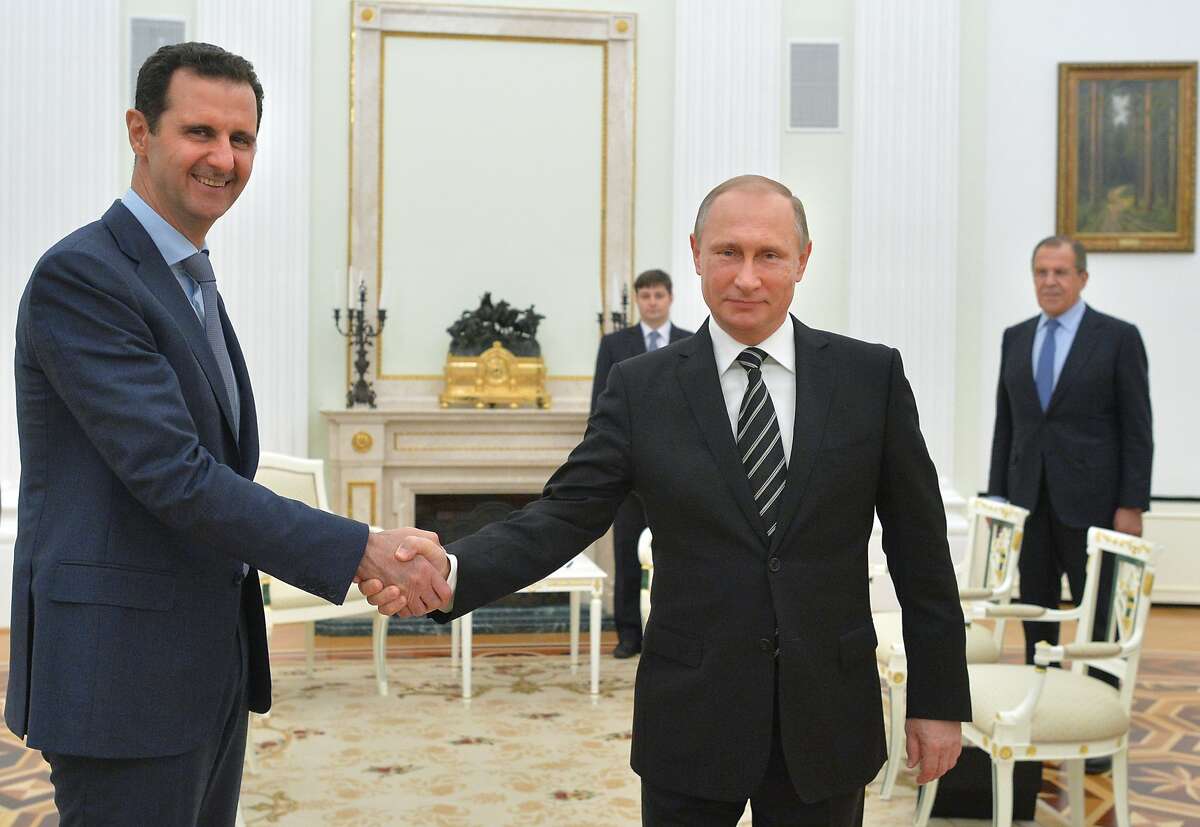 FILE - In this file photo taken on Tuesday, Oct. 20, 2015, Russian President Vladimir Putin, center, shakes hand with Syrian President Bashar Assad as Russian Foreign Minister Sergey Lavrov, right, looks on in the Kremlin in Moscow, Russia. Syria's state news agency is quoting President Bashar Assad as saying that the Russian military will draw down its air force contingent from Syria but won't leave the country altogether.(Alexei Druzhinin, Sputnik, Kremlin Pool Photo via AP, File)