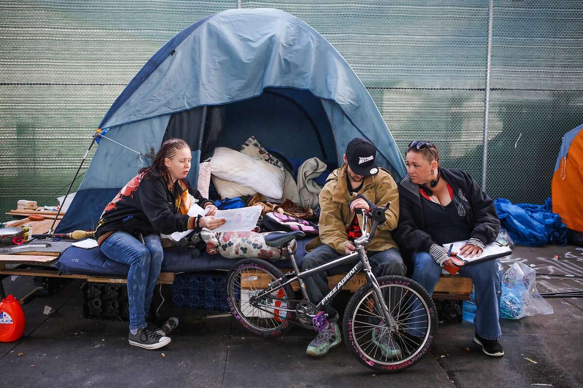 Joolie Coombes (left), Jeremy Harvell and a member of the Homeless Outreach Team are gathered outside a homeless camp tent on Division Street in San Francisco in March 1.