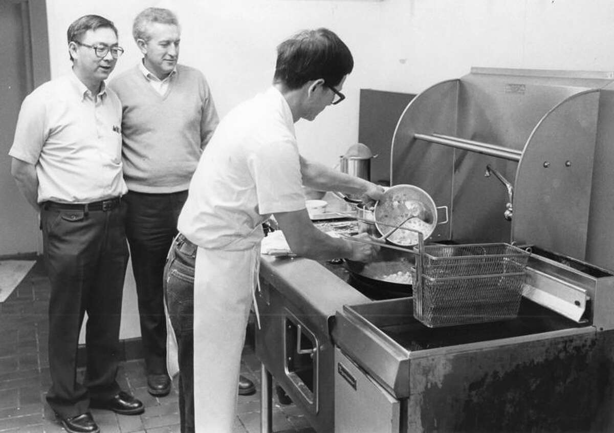 Carl Chow, left, and Larry Wegner watch Jack Hu prepare a wok full of almond chicken at their new Chinese fast-food restaurant.