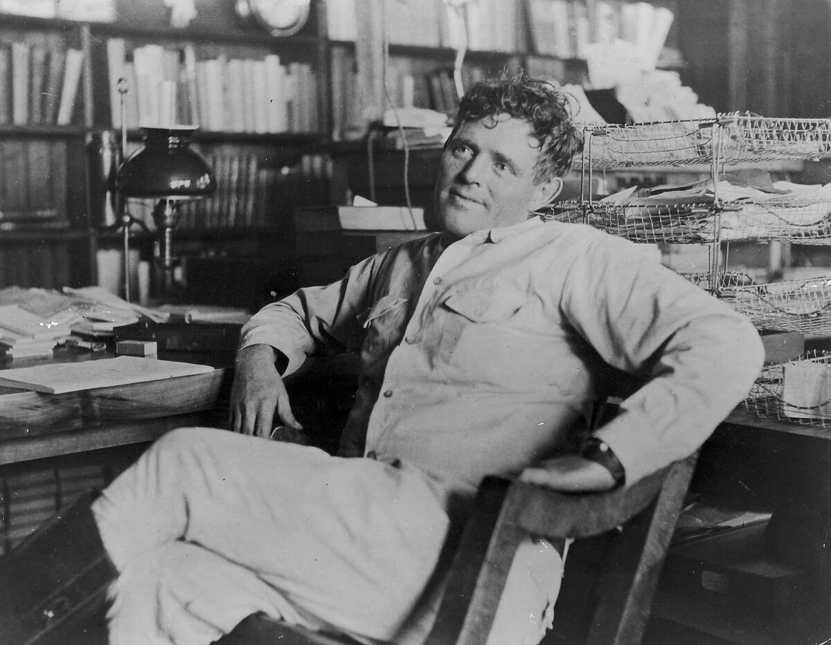 American author Jack London (1876-1916) reclines next to his desk in a wooden chair, smiling, his legs crossed. (Photo by Hulton Archive/Getty Images)