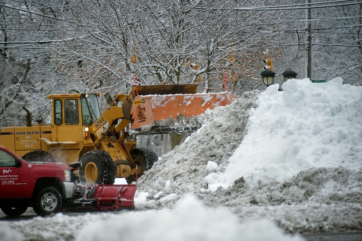 Crews work to remove snow from the parking lot at the corner of Ellsworth and Ashman streets in Midland on Sunday after a snow storm hit the area.