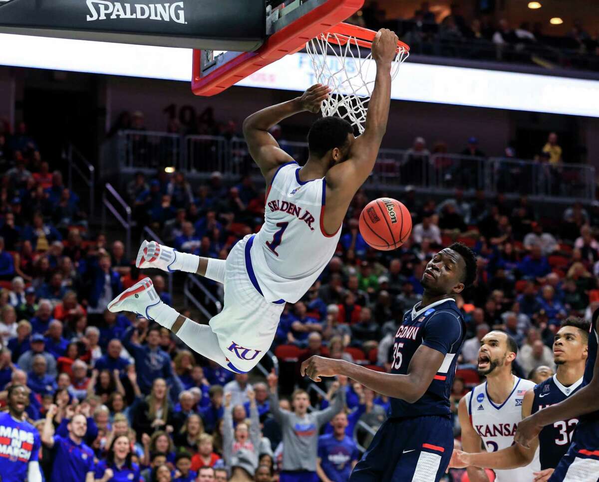 Kansas' Wayne Selden Jr. (1) hangs on to the rim after dunking over Connecticut's Amida Brimah (35), with Perry Ellis (34) and Shonn Miller (32) watching, during a second-round men's college basketball game in the NCAA Tournament in Des Moines, Iowa, Saturday, March 19, 2016. Kansas won 73-61.