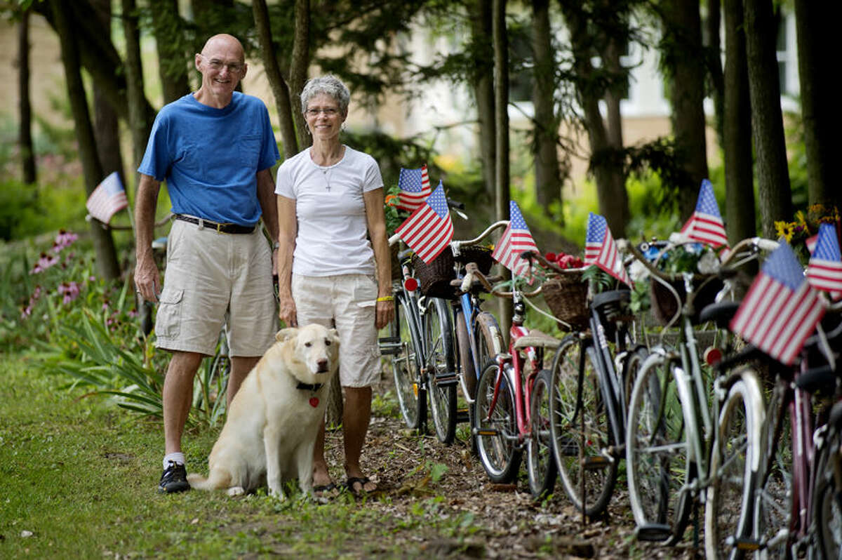  Sherryand Larry Jacobs pose with their dog Nya in front of their "bicycle fence" on their property in Midland.