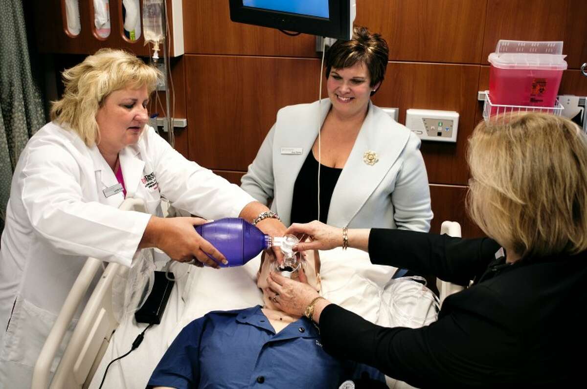 Davenport University faculty member Lynette Love, left, uses a bag valve mask on “Sim Man” with the help of Provost Linda Rinker, right, while nursing faculty member Amy Stahley, center, looks on Monday afternoon at the unveiling of the new simulation labs at the Midland campus. “‘Sim Man’ offers students the ability to practice situations they may encounter in a clinical environment in a safe learning environment,” said Shannon Krolikowski, simulation lab and clinical coordinator.