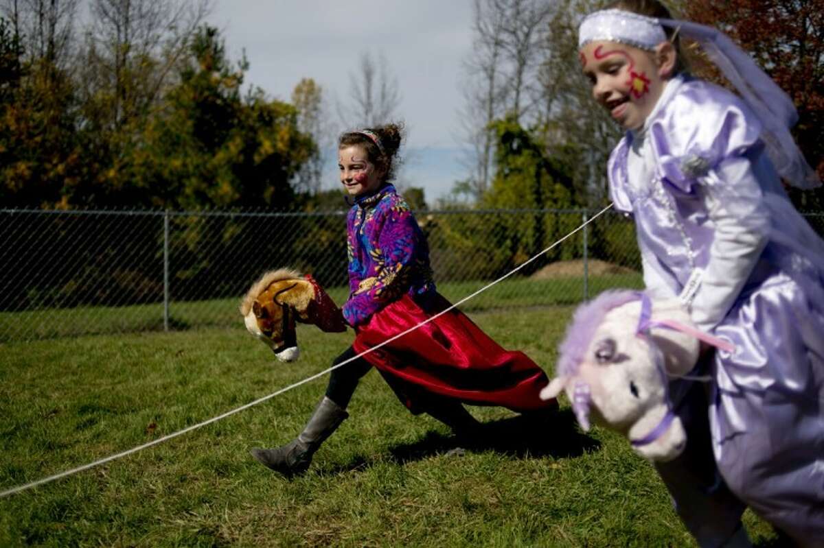 NEIL BLAKE | nblake@mdn.netMidland Academy for Advanced and Creative Studies first-grader Ella Simpson, left, rides "George" and first-grader Kennedi Kickbusch rides "Buttercup" as they race each other at the Renaissance Festival at the school on Friday.