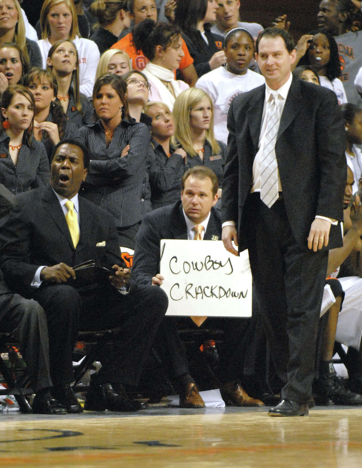 Oklahoma State assistant coach Kyle Keller, center, flanked by assistant coach Jimmy Williams, left, and head coach Sean Sutton, right, holds up a whiteboard for Oklahoma State players during overtime of an NCAA college basketball game in Stillwater, Okla., Tuesday, Jan. 16, 2007. Oklahoma State defeated Texas in triple overtime 105-103.(AP Photo/Brody Schmidt)