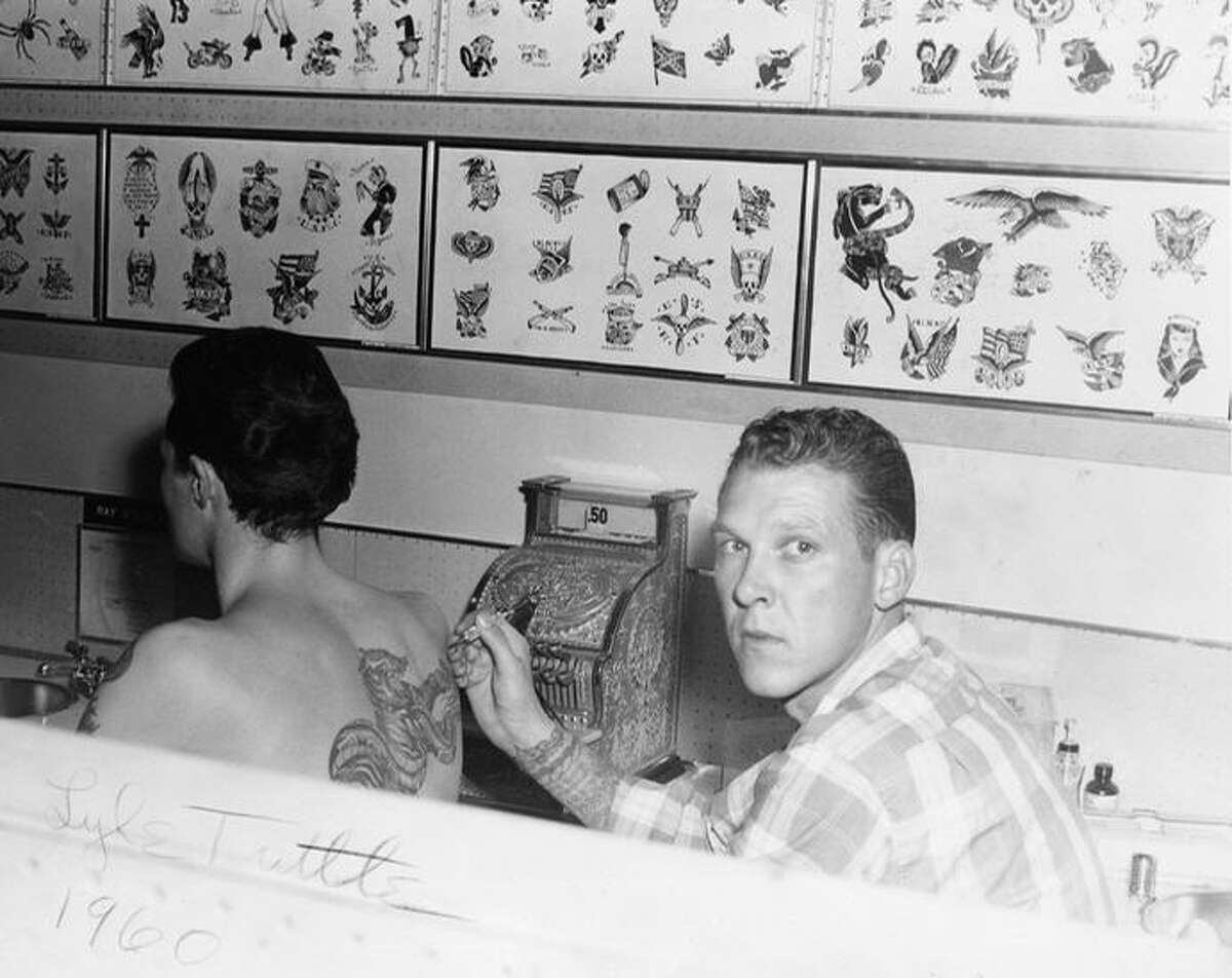 Tuttle tattooing in the early '60s. Notice the flash on the walls behind him. 