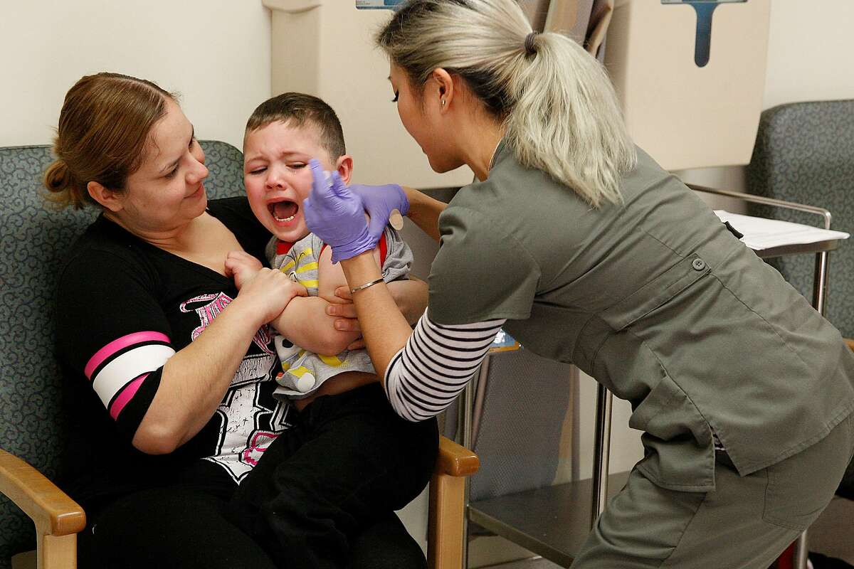 Elsa Sandoval-Anguiano from East Palo Alto comforts her son Damian Anguiano (middle), 4 years old, while he receives the MMRV-measles, mumps , rubella, varicella-- vaccine at the Kaiser pediatric immunization clinic in Redwood City, Calif., on Friday, January 23, 2015. 