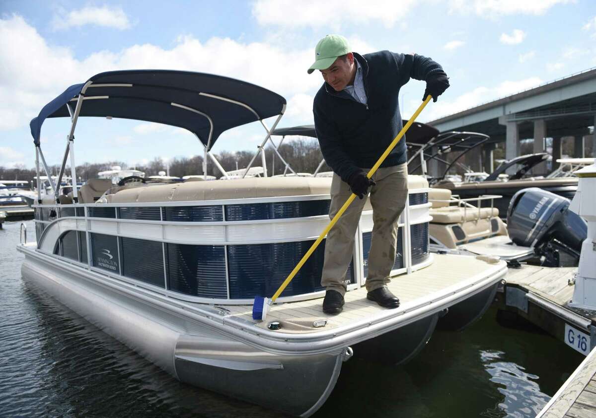 Above, John Benchimol, president of Harborside Marina & Yacht Sales, cleans snow and ice off of a Bennington pontoon boat at the Greenwich Boat Show at the Greenwich Water Club on Sunday. Below, folks browse at the boat show.