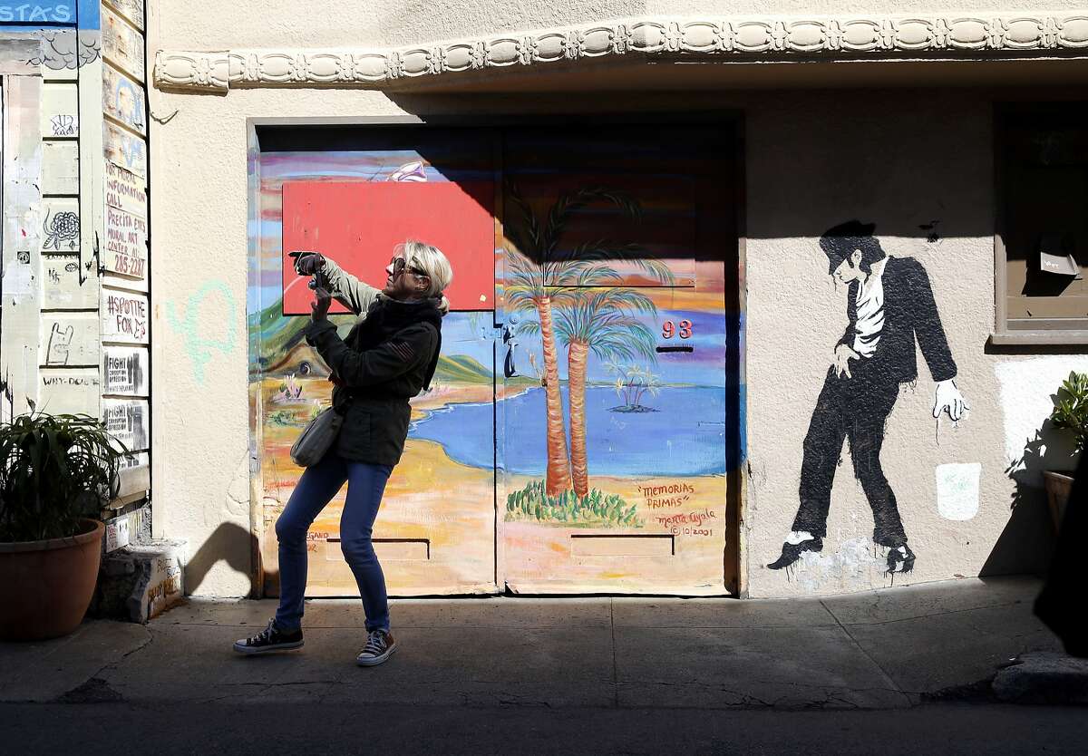 A woman takes a photograph of a mural with her phone during a tour of the Mission District for attendees of the Association of American Geographers annual conference in San Francisco, California, on Thursday, March 31, 2016.
