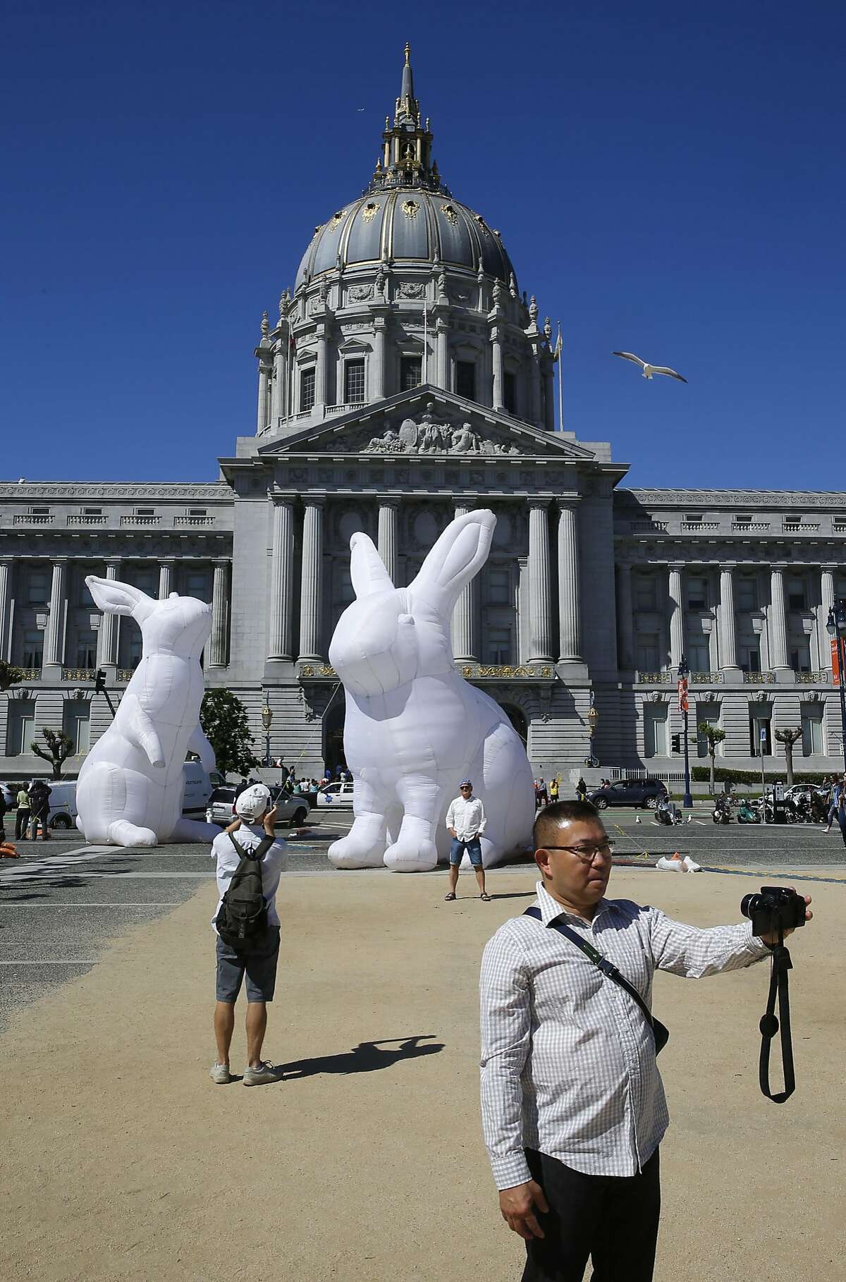 Cesar Ejerta of San FRancisco stops for a photo in front of Australian artist Amanda Parer's installation 'Intrude,' featuring five 23-foot-tall inflated nylon rabbits, is touring the country and is currently on display in San Francisco's Civic Center Plaza, on Tues. April 5, 2016.