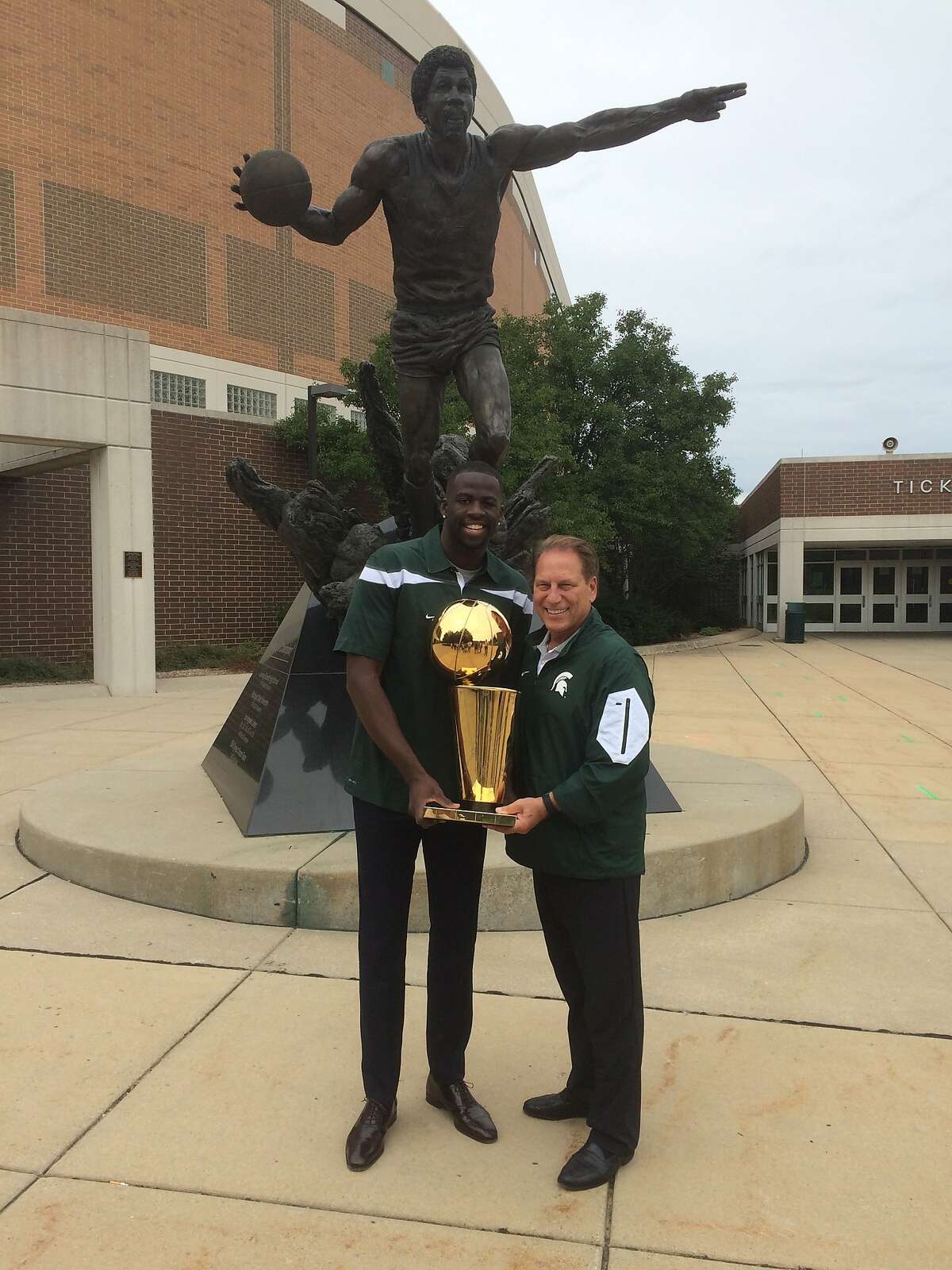 Draymond Green and Michigan State coach Tom Izzo pose with the Larry O'Brien trophy in front of the Magic Johnson statue at the East Lansing, Mich., school.