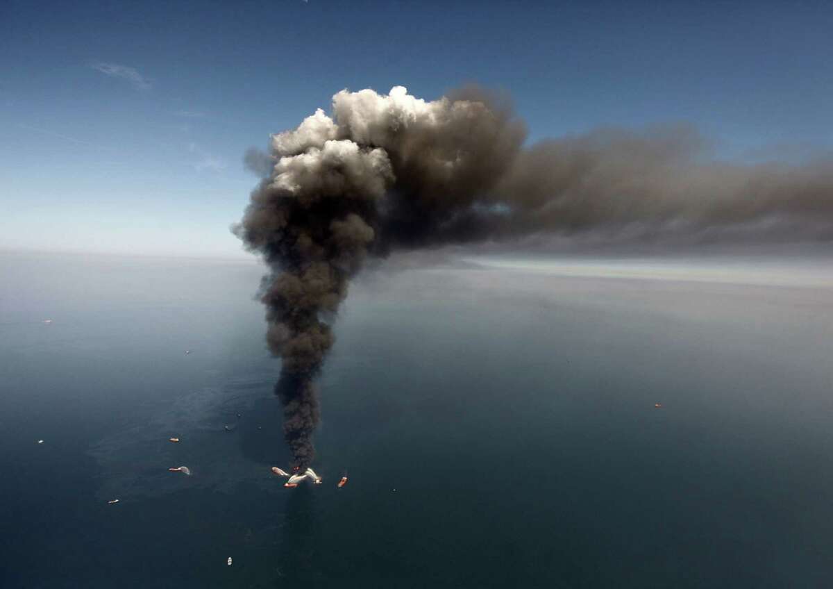 In this Wednesday, April 21, 2010 file photo, oil can be seen in the Gulf of Mexico, more than 50 miles southeast of Venice on Louisiana's tip, as a large plume of smoke rises from fires on BP's Deepwater Horizon offshore oil rig. An April 20, 2010 explosion at the offshore platform killed 11 men, and the subsequent leak released an estimated 172 million gallons of petroleum into the gulf. (AP Photo/Gerald Herbert, File)