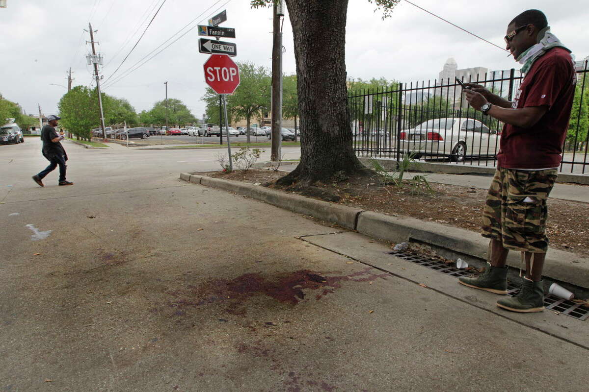 Ariel Johnson photographs the blood stains on Dennis Street where a double homicide happen Monday, April 11, 2016, in Houston's Midtown. Police were called Dennis Street in the early-morning hours Monday and found two men shot and beaten.