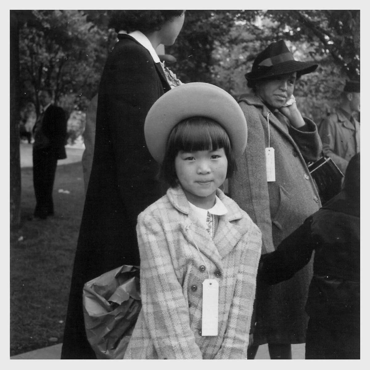 Dressed in her best clothes, Mae Yanagi, 7, waits with her pregnant mother, Kinuye Yanagi, right, to be bused to housing in the Tanforan Assembly Center by the War Relocation Authority. The Yanagi family spent several months in a horse stall at Tanforan before being sent to the Topaz Internment Camp in the Utah desert. Hayward, California. Photograph by Dorothea Lange.5/ 8/ 42