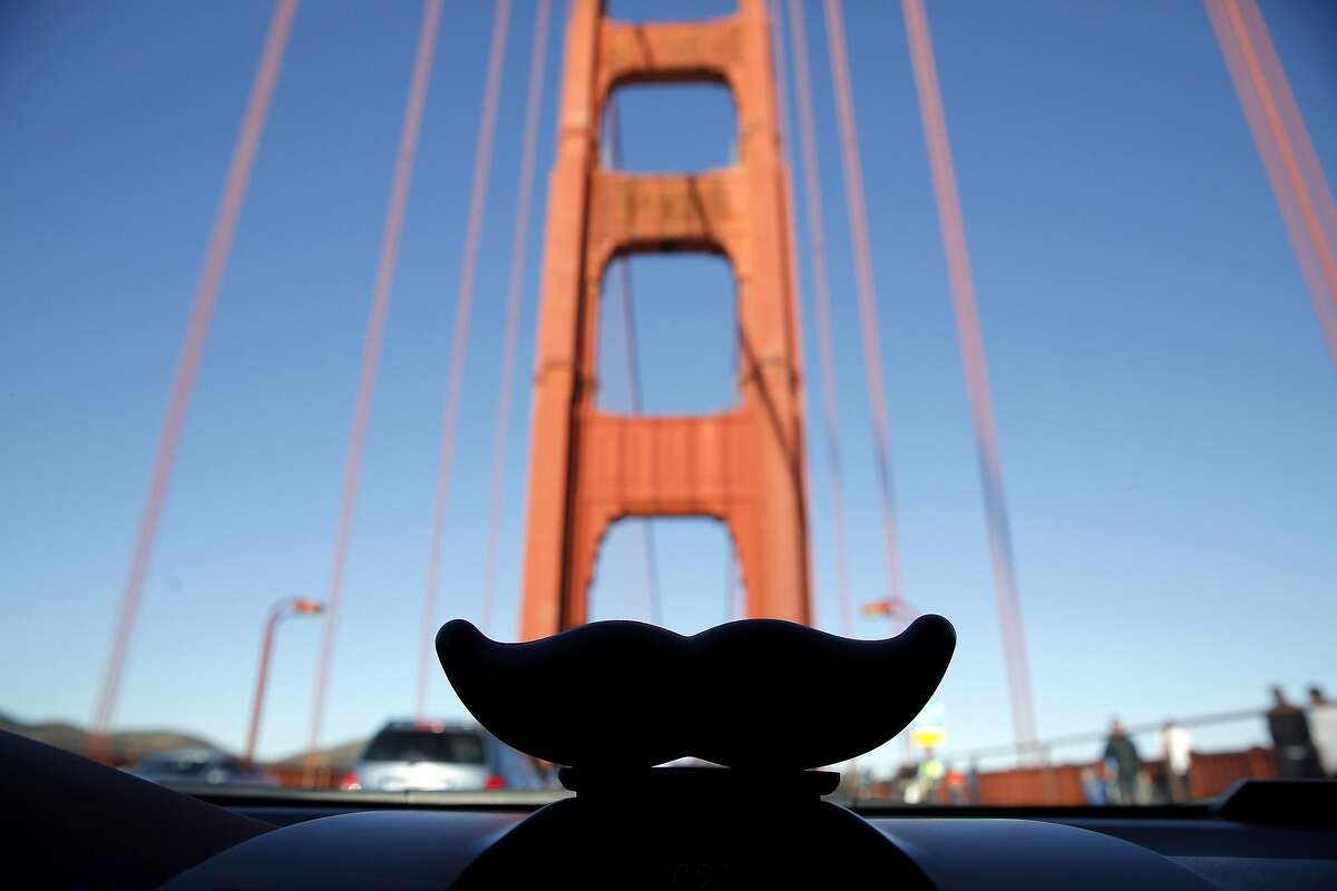 A Lyft mustache on a car dashboard in front of the Golden Gate Bridge near San Francisco, California, on Tuesday, Dec. 29, 2015.