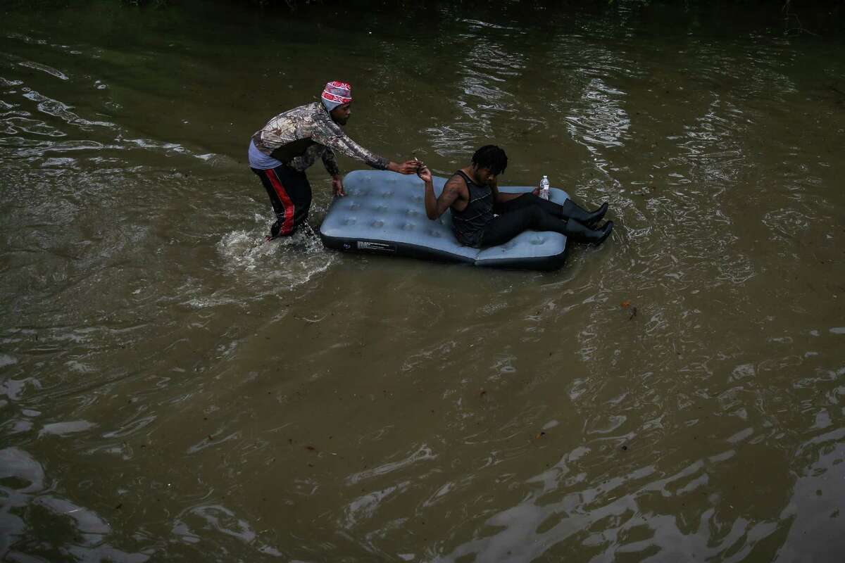 A man riding on an inflatable mattress passes a cigarette to the man pushing as they navigate the flooded Greenspoint area Monday, April 18, 2016 in Houston.