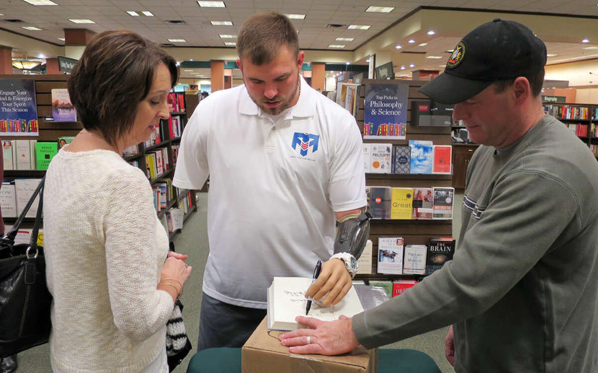 Retired Army Staff Sgt. Travis Mills, center, signs a book for Lori Jones, left, of Unity, Maine, whose husband became ill and died after a deployment to Iraq, at an event promoting Mills' book, "Tough As They Come," on Tuesday, Dec. 1, 2015, in Augusta, Maine. Mills, who lives in Manchester, Maine, lost all four limbs as a result of an IED blast in 2012 in Afghanistan. (AP Photo/David Sharp)