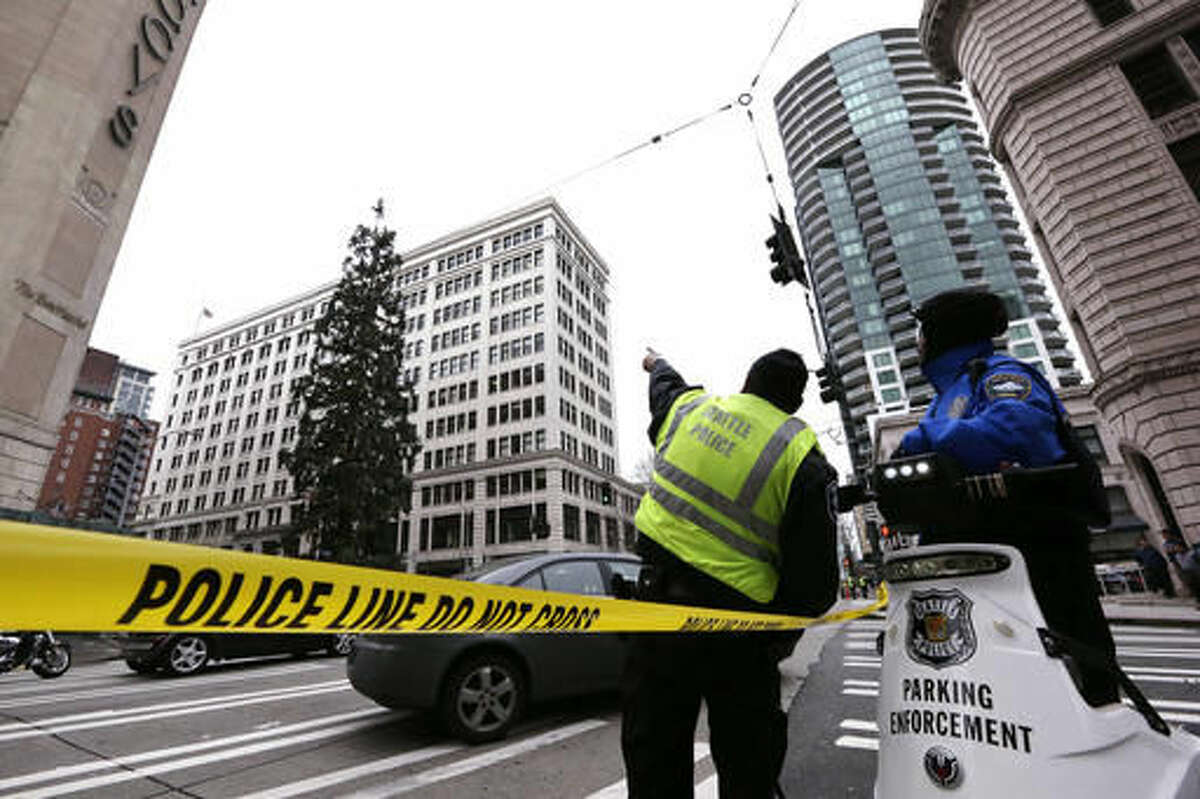 Police look across the street and up at an 80-foot tall sequoia tree where a man continues to perch near the top Wednesday morning, March 23, 2016, in downtown Seattle. Authorities were alerted to the unidentified man in the tree around 11 a.m. Tuesday and he was still clinging to its branches nearly a day later. The man, name and cause unknown, has transfixed the city and the Internet over the past two days as his action prompted police to close adjacent streets and as negotiators tried to coax him down. (AP Photo/Elaine Thompson)