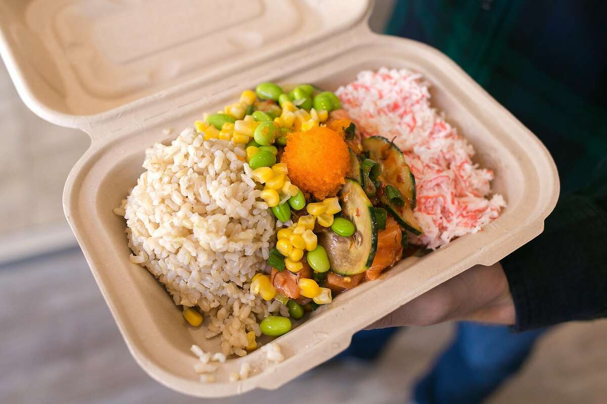 A customer holds his bowl of brown rice, edamame, corn, tuna, and crab salad.