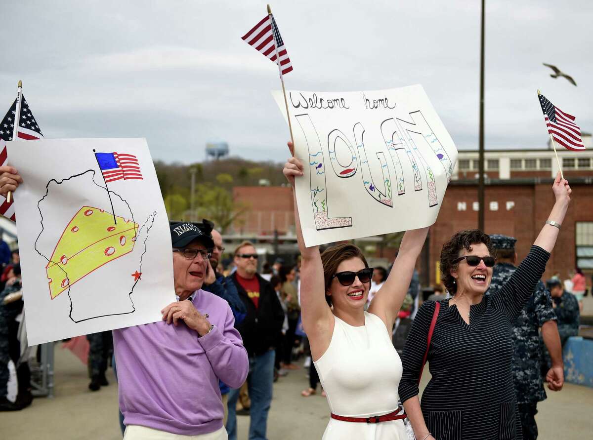 Kelsey McManus, center, flanked by her future in-laws Tom and Ann Roy, waves a banner to attract her fiancee Lt. j.g. Logan Roy as the U.S. Navy submarine USS Toledo (SSN 769) returns to the Navy Submarine Base in Groton, Conn., Monday, April 25, 2016, following a six-month deployment. The Toledo visited ports in Bahrain, France, Spain and Greece. 