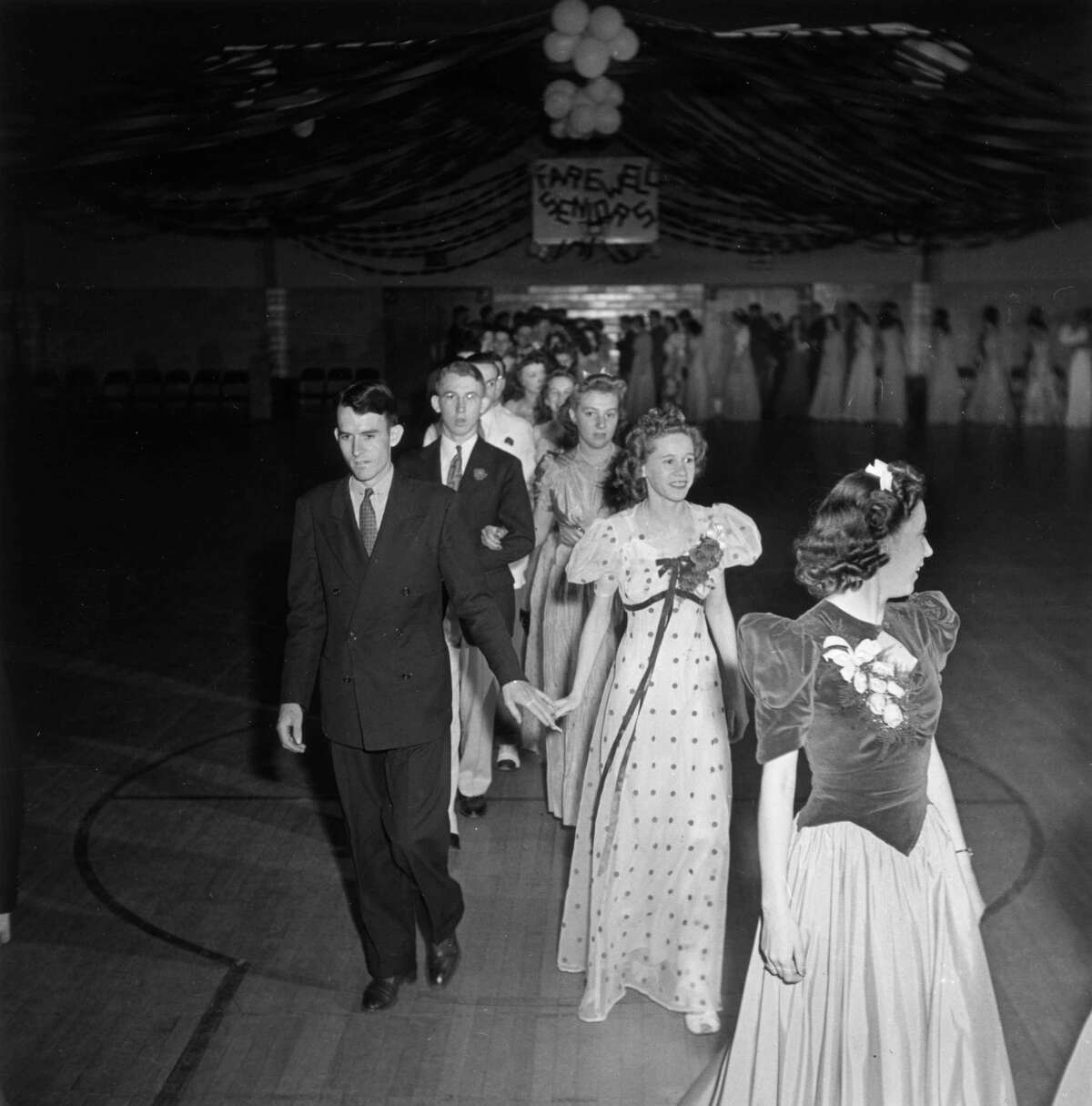 1942: High school seniors cross a gymnasium floor in a double file line at their prom dance, Greenbelt, Maryland.