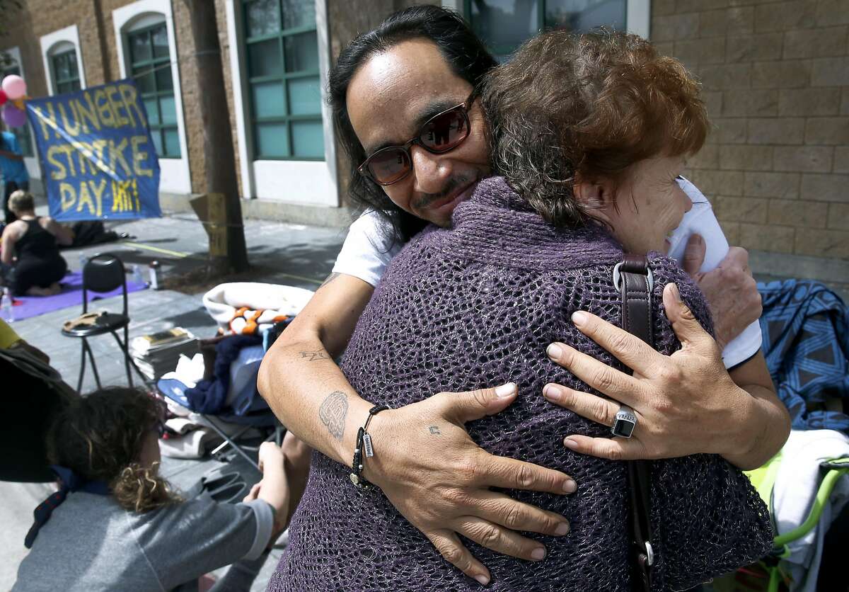 Ilyich Sato, who's known as the rapper Equipto, hugs longtime family friend Naomi White as a hunger strike continues in front of the Mission police station on Valencia Street in San Francisco, Calif. on Tuesday, April 26, 2016. Activists are calling for Chief Greg Suhr to resign after a number of fatal officer involved shootings.